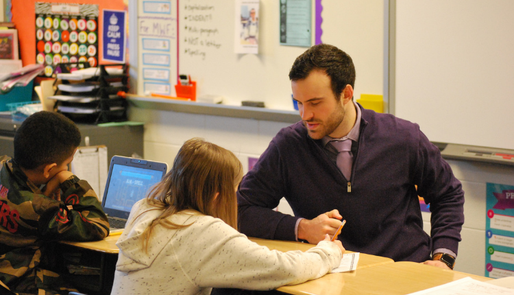 male teacher working at a desk with two young students